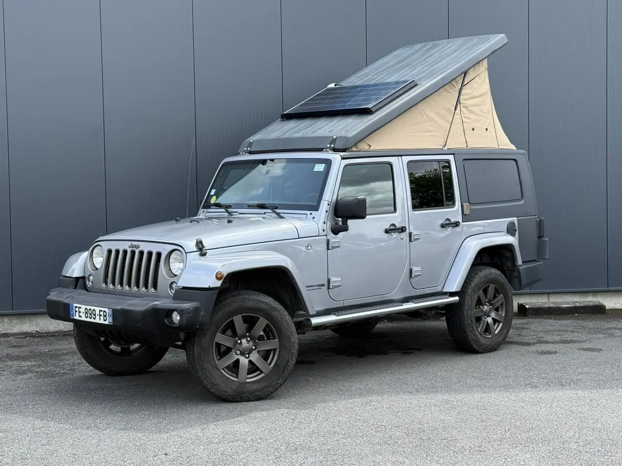Jeep Wrangler Billet Silver vue 3/4 avant droit avec toit relevable beige et panneau solaire intégré.