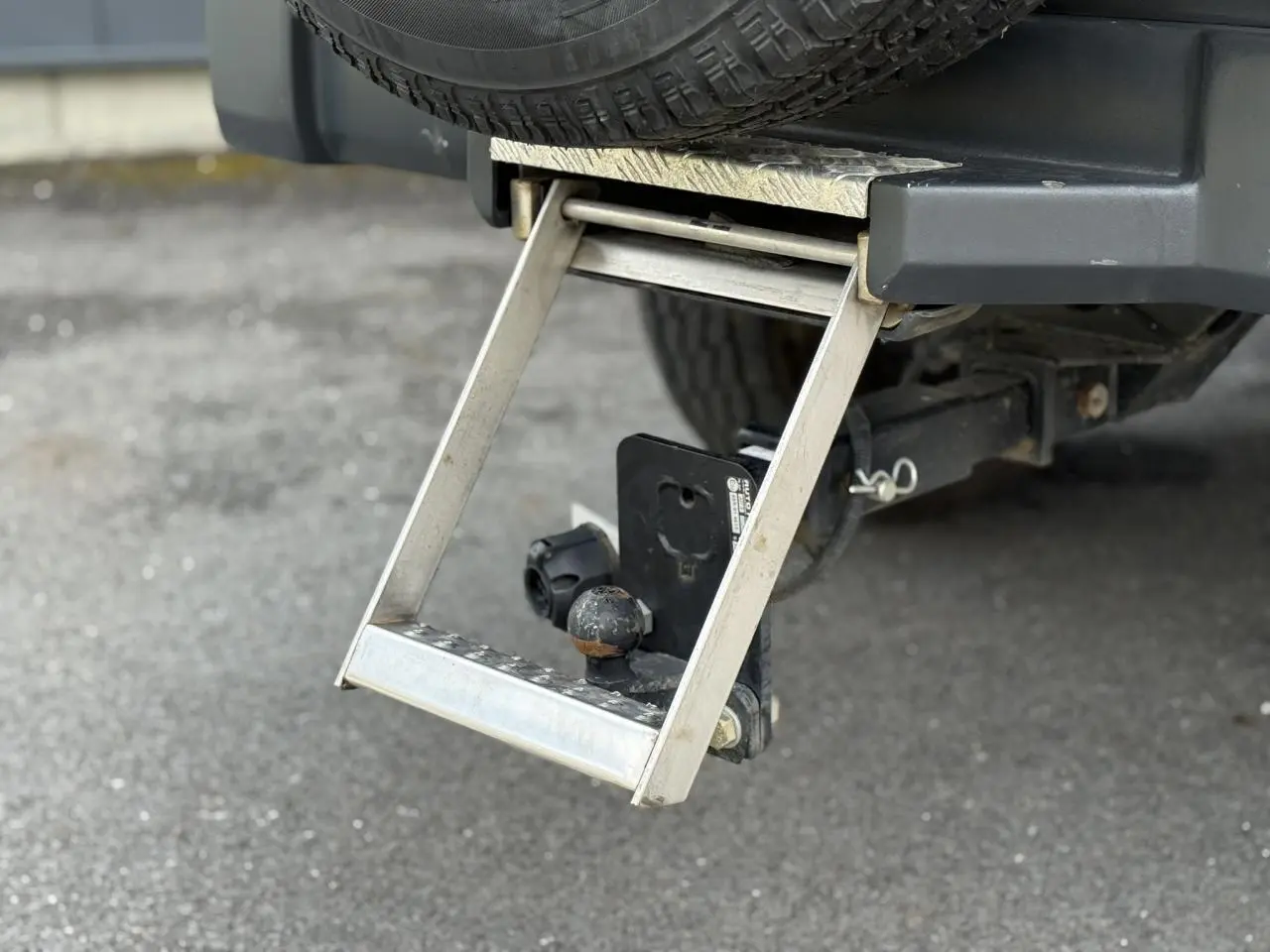 Gros plan sur l'attelage et la marche-pieds arrière du Jeep Wrangler Billet Silver, avec roue de secours visible.