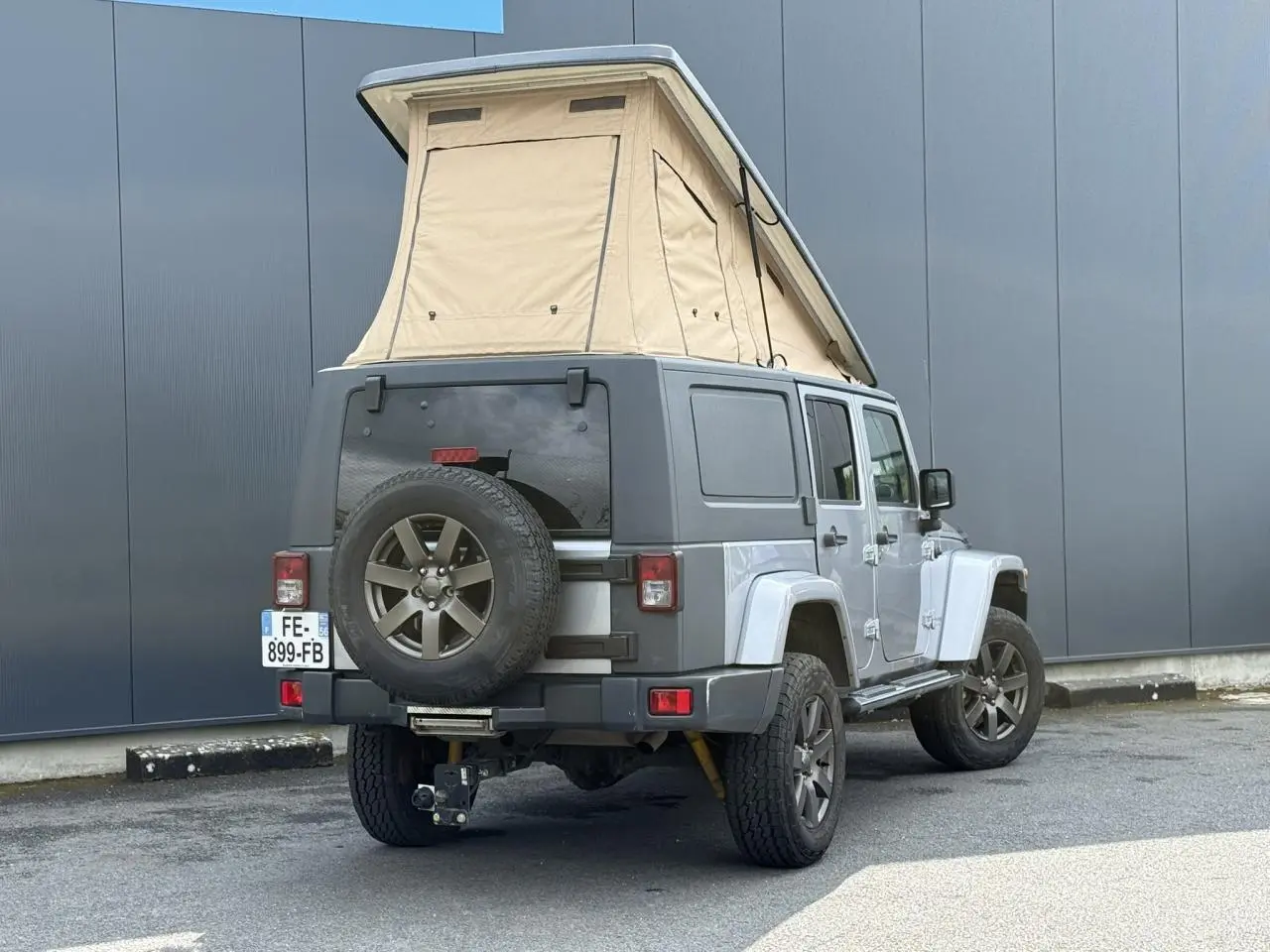 Vue 3/4 arrière droite du Jeep Wrangler Billet Silver avec toit relevable beige et roue de secours sur hayon.