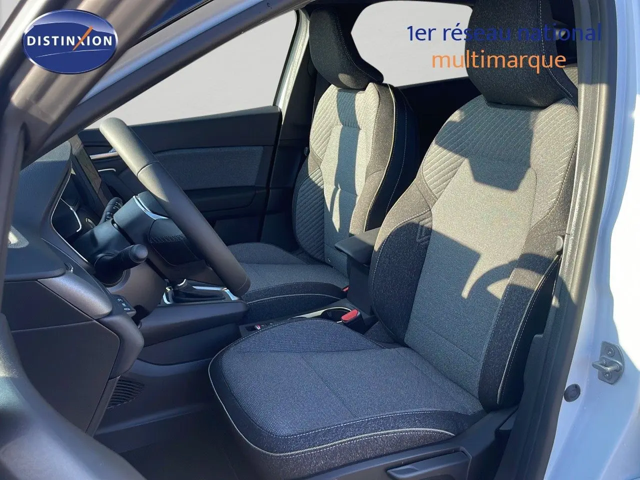 Intérieur avant du Renault Captur blanc nacré, sièges tissu noir et gris avec volant et console visibles.