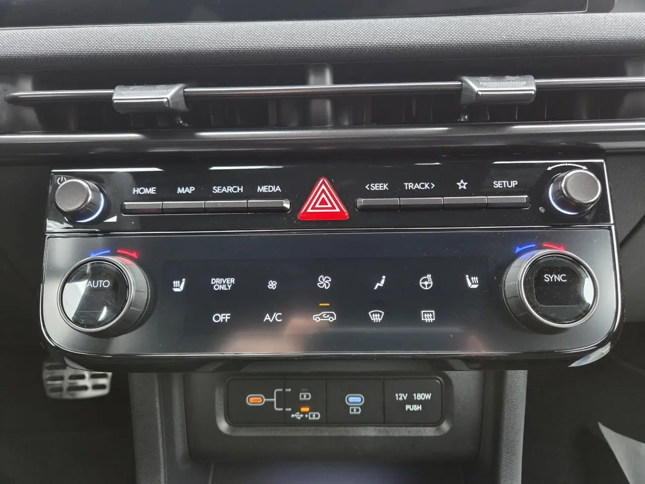 Vue rapprochée de la console centrale noire brillante du Hyundai Tucson 2025, avec commandes climatisation et multimédia.