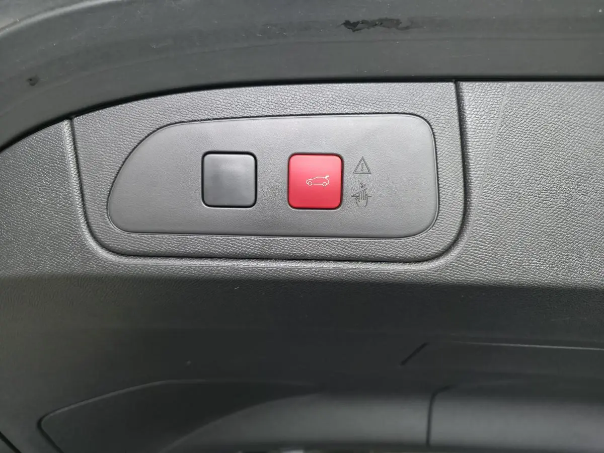 Gros plan sur les boutons du hayon motorisé, dont un rouge avec pictogramme de coffre, intérieur noir.
