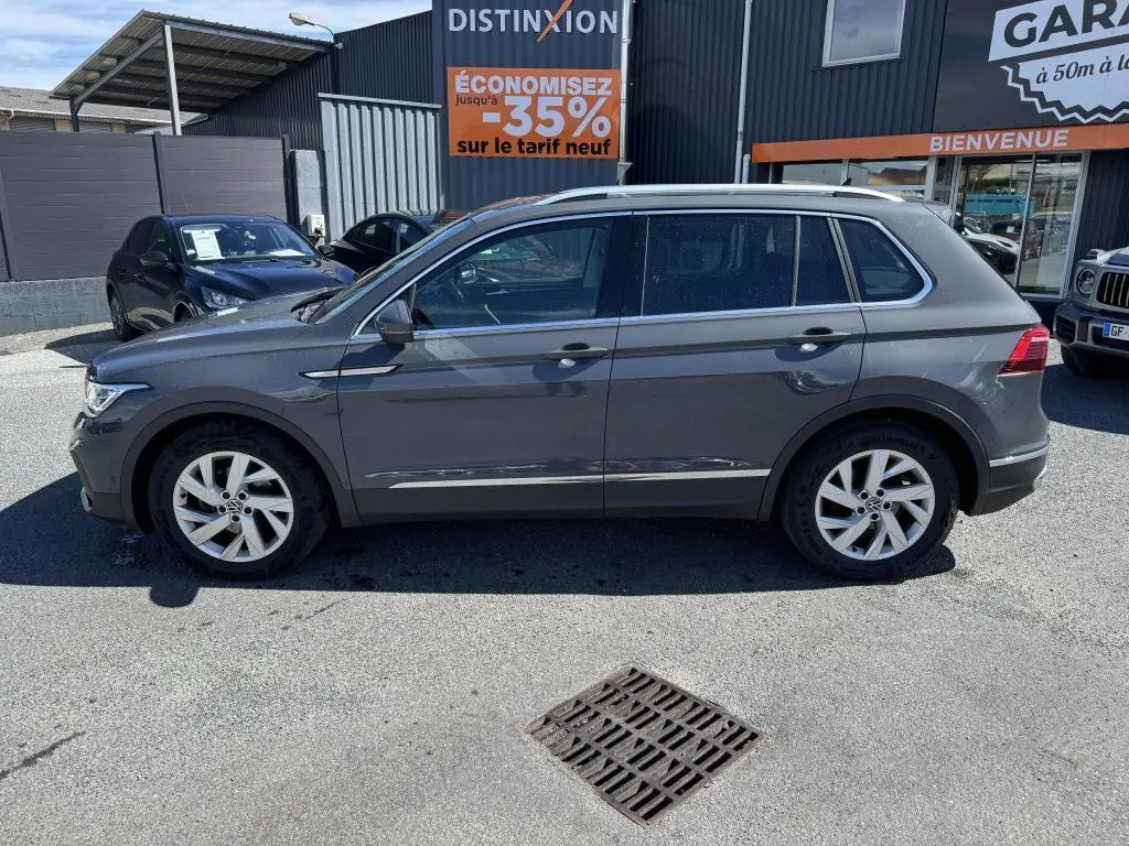 Profil côté gauche d'un Volkswagen Tiguan gris 2021 garé devant un garage avec jantes alliage 18 pouces.