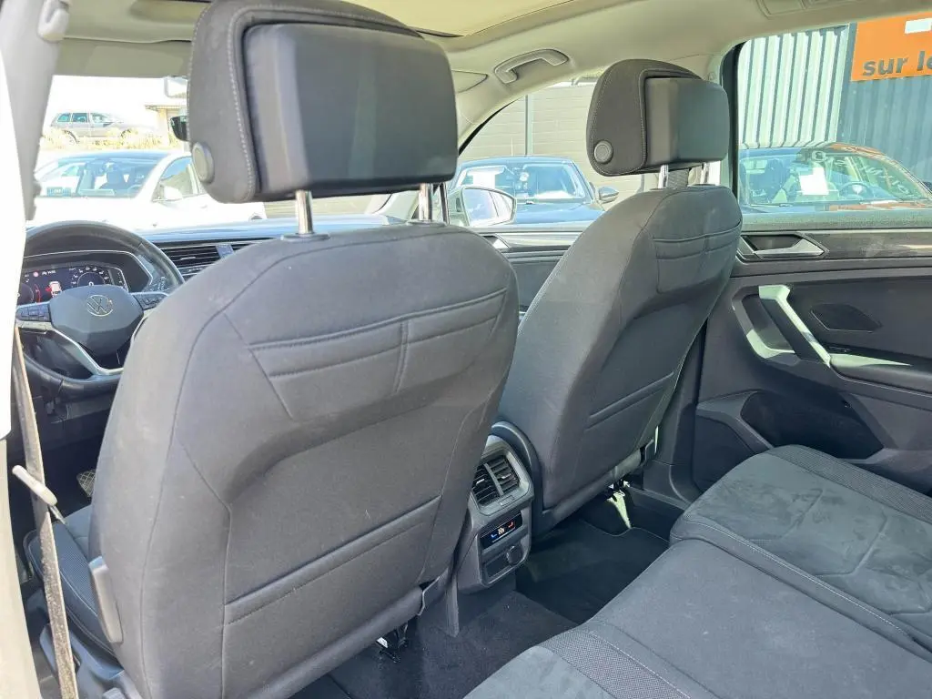 Vue intérieure arrière du Volkswagen Tiguan 2.0 TDI gris, montrant les sièges avant en tissu noir et la console centrale avec commandes climatisation.