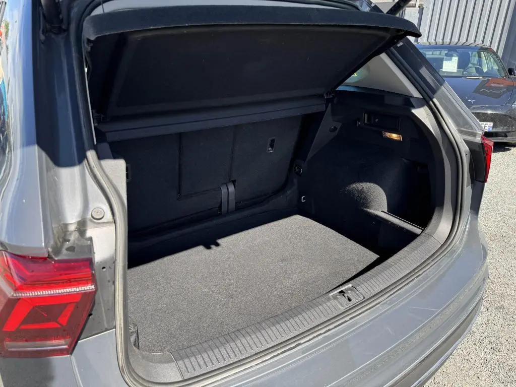 Coffre ouvert côté arrière droit d’un Volkswagen Tiguan 2.0 TDI gris, montrant un espace de chargement propre et spacieux.