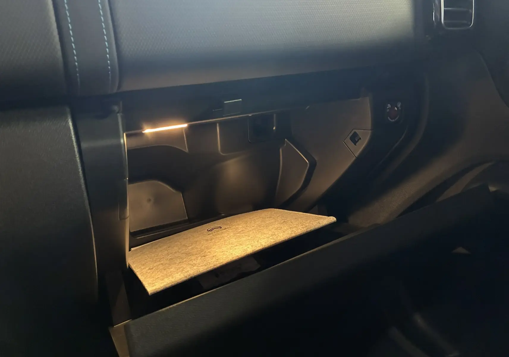 Gros plan sur la boîte à gants ouverte du Citroën C5 Aircross 2025, intérieur noir avec éclairage intérieur doux.