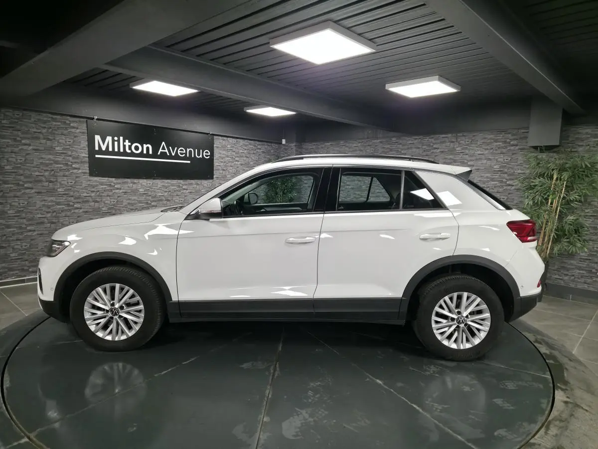 Profil côté gauche d'un Volkswagen T-Roc blanc 2022 avec jantes alliage et toit noir en showroom.