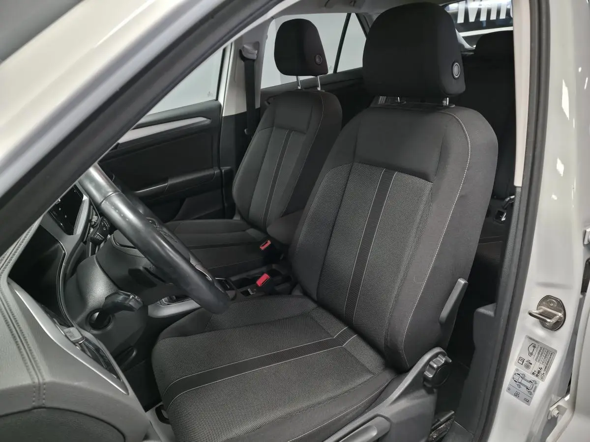 Intérieur côté gauche du Volkswagen T-Roc blanc 2022, sièges avant en tissu noir avec coutures grises visibles.