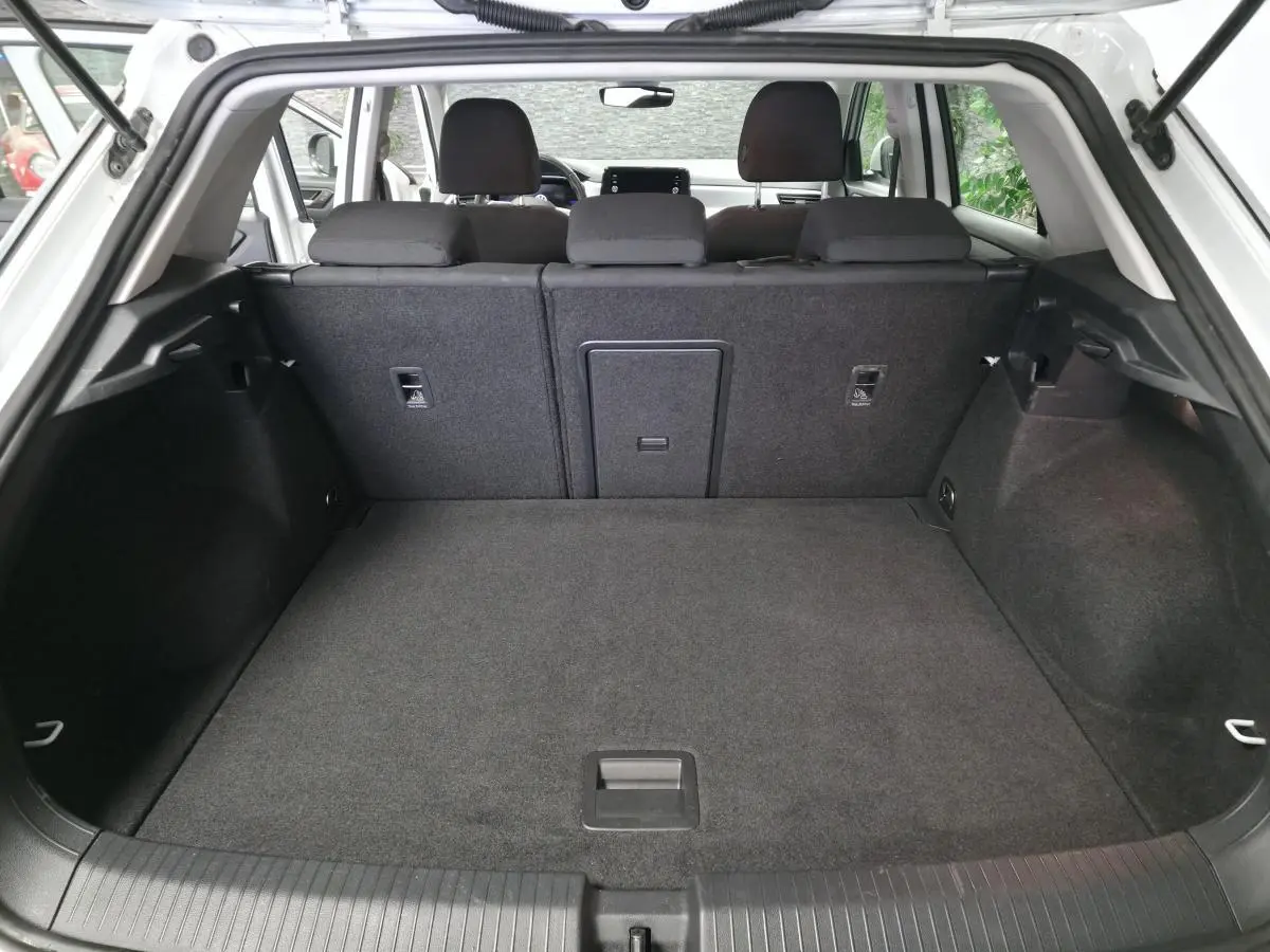 Coffre ouvert du Volkswagen T-Roc blanc, vue arrière montrant l'espace de chargement et les sièges arrière rabattus partiellement.