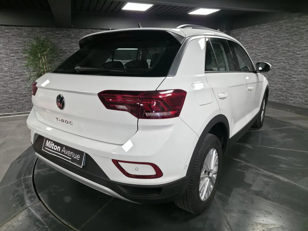Vue 3/4 arrière droite d'un Volkswagen T-Roc blanc avec feux arrière LED et jantes alliage 16 pouces dans un showroom.