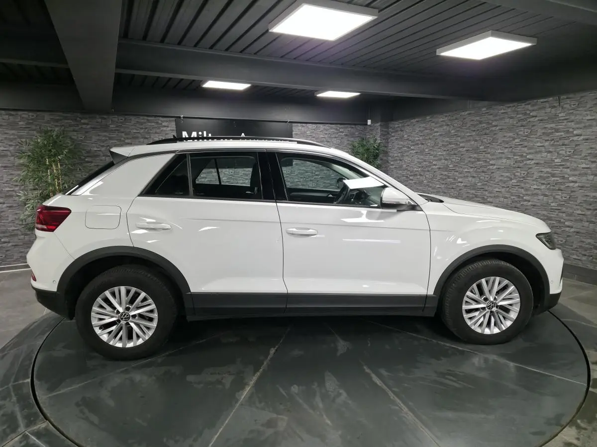 Volkswagen T-Roc blanc vu de profil côté gauche, avec jantes alliage 16 pouces et toit noir contrasté.