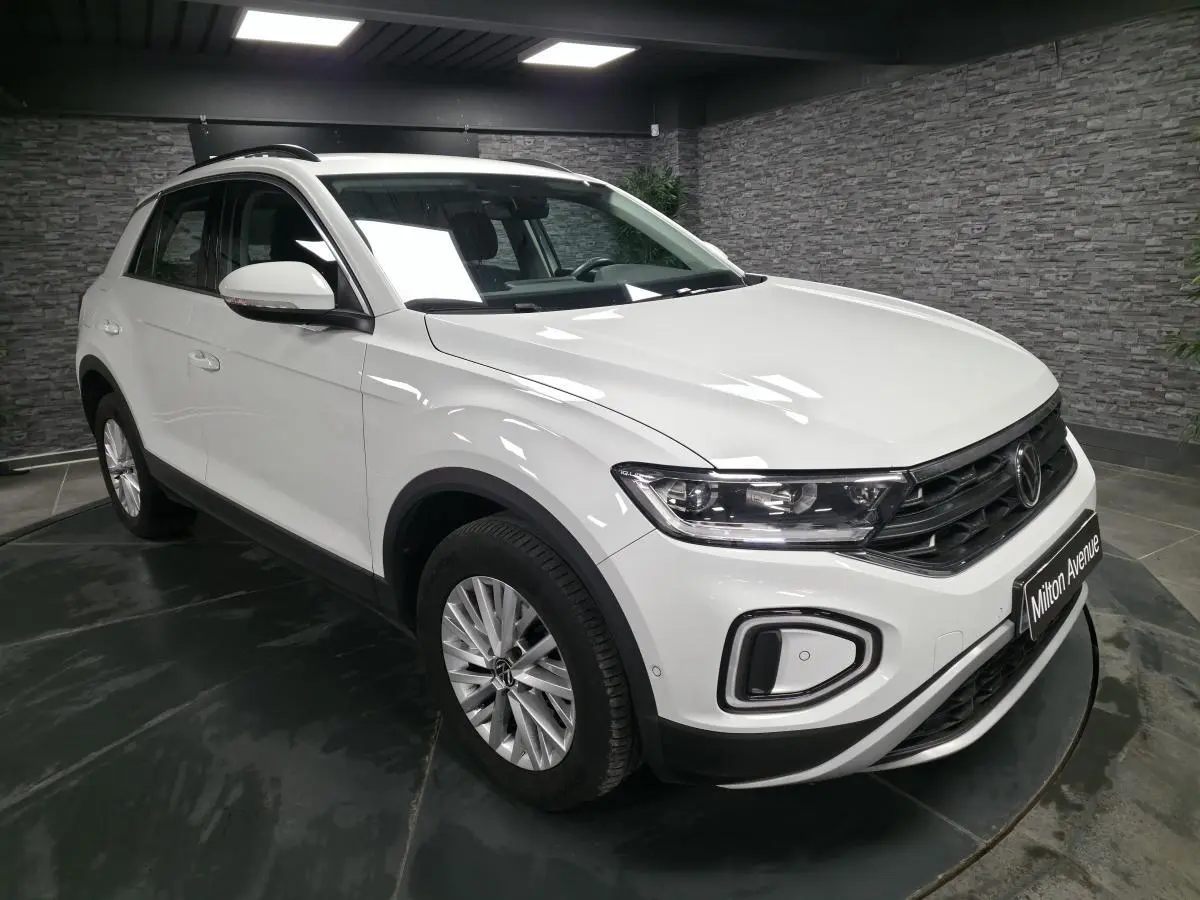 Volkswagen T-Roc blanc vue 3/4 avant droit en intérieur avec jantes alliage et feux LED circulaires.