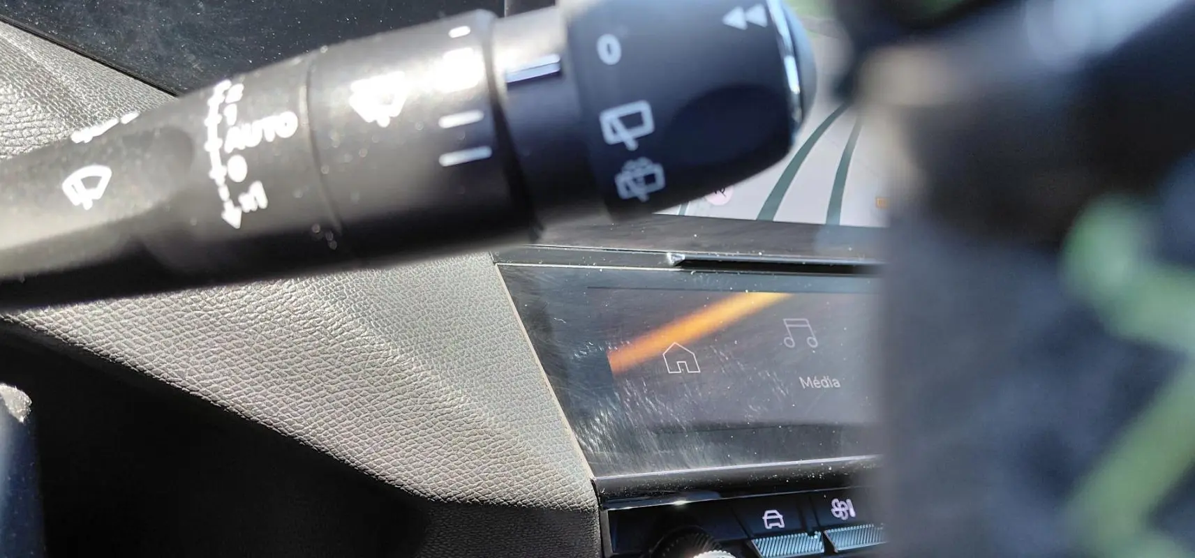 Détail du commodo de commandes et partie de l’écran tactile du tableau de bord dans l’habitacle d’une Peugeot 308 Hybrid gris.