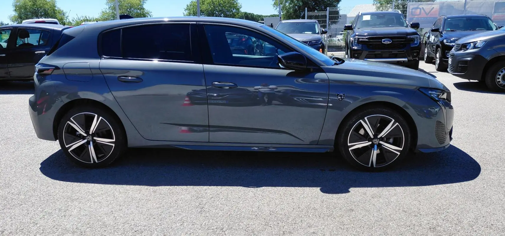 Profil côté gauche d'une Peugeot 308 Hybrid 145 e-DCS6 GT gris avec jantes alliage 18 pouces sur parking extérieur.