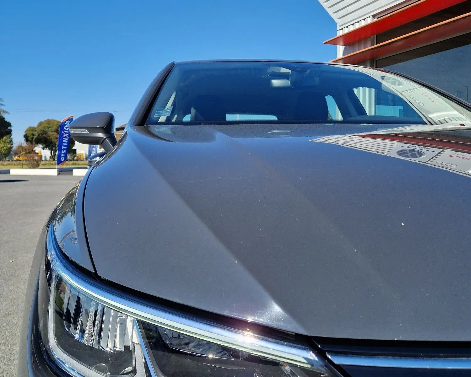 Gros plan sur l'avant gauche d'une Volkswagen Golf A8 gris Urano, mettant en valeur le phare et la calandre sous un ciel bleu.