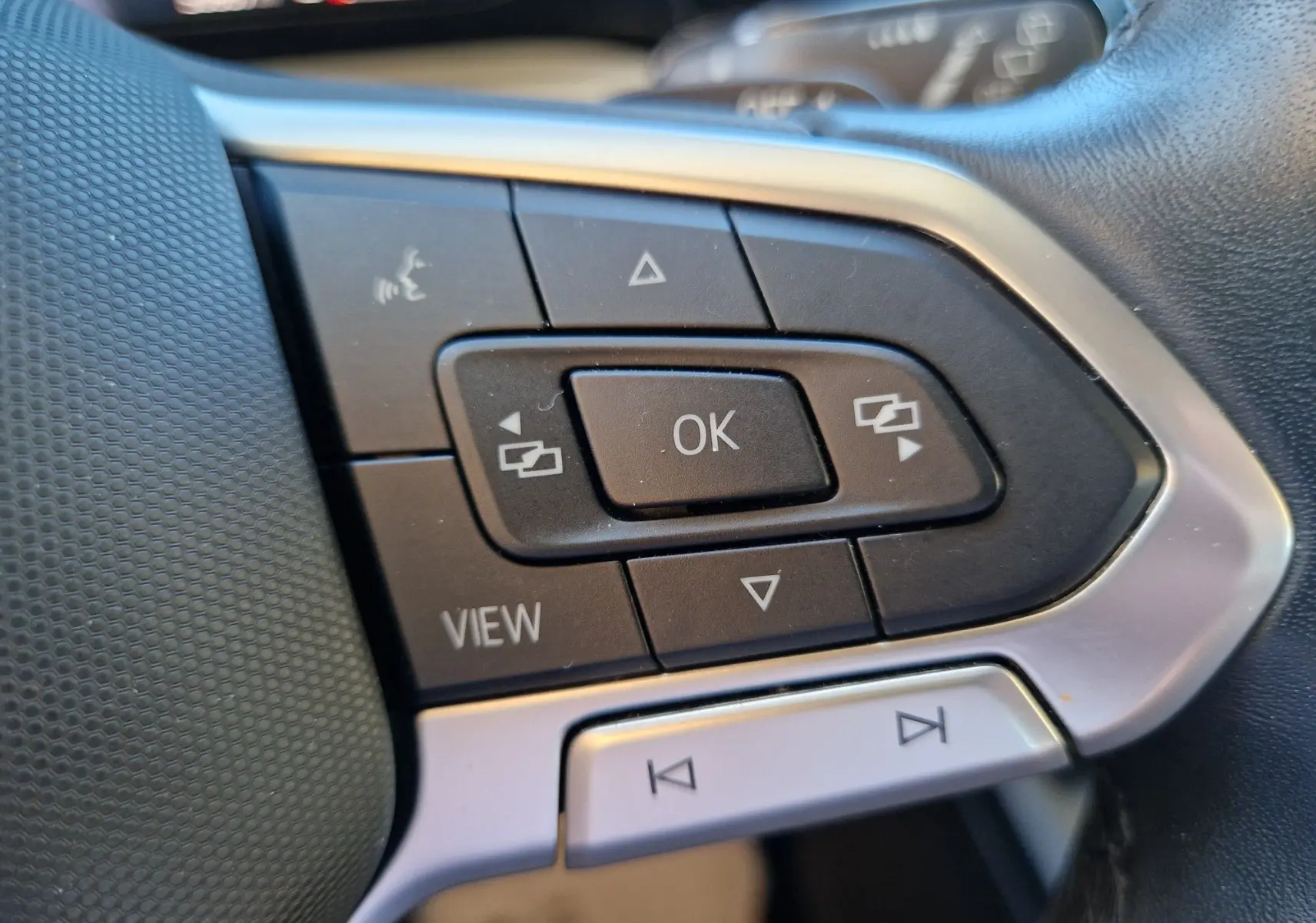 Gros plan sur les commandes multifonctions noires et argentées du volant côté gauche d'une Volkswagen Golf gris Urano 2023.