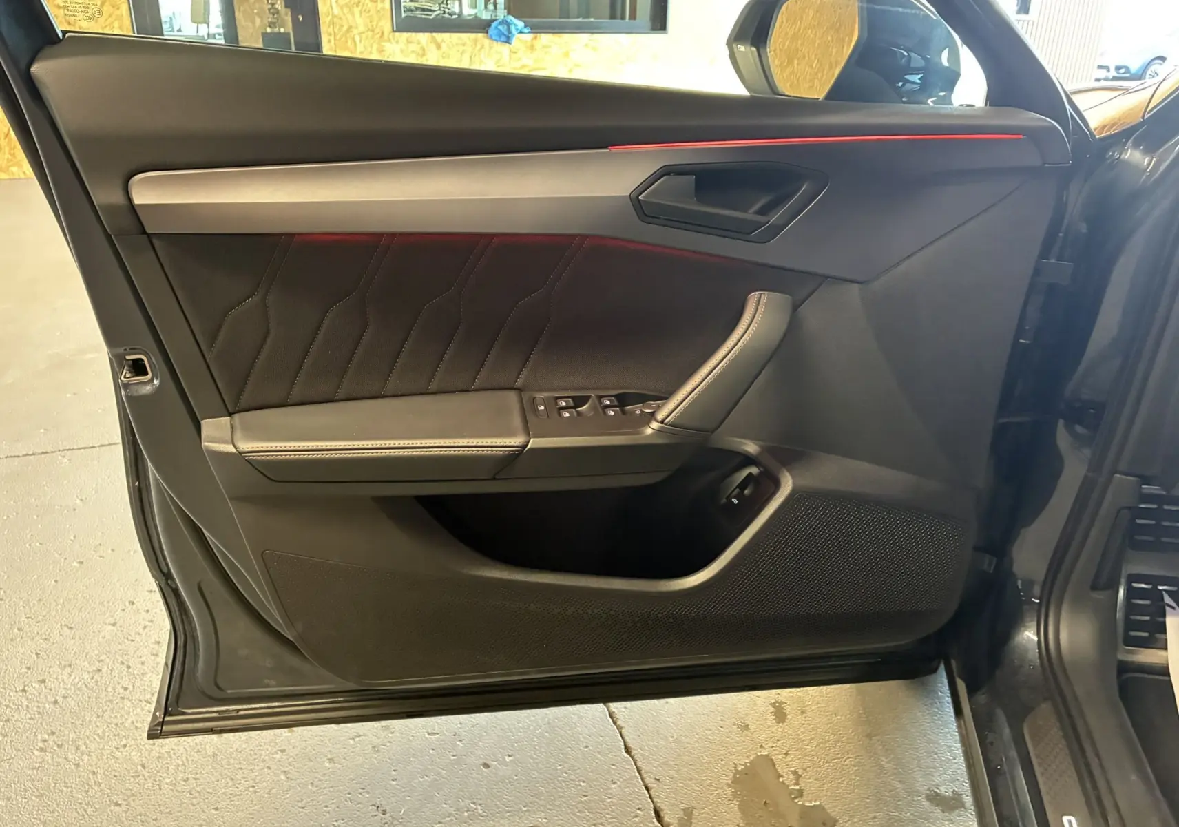 Porte avant gauche ouverte d'une CUPRA Formentor gris foncé, montrant le panneau intérieur noir avec surpiqûres et bande rouge discrète.