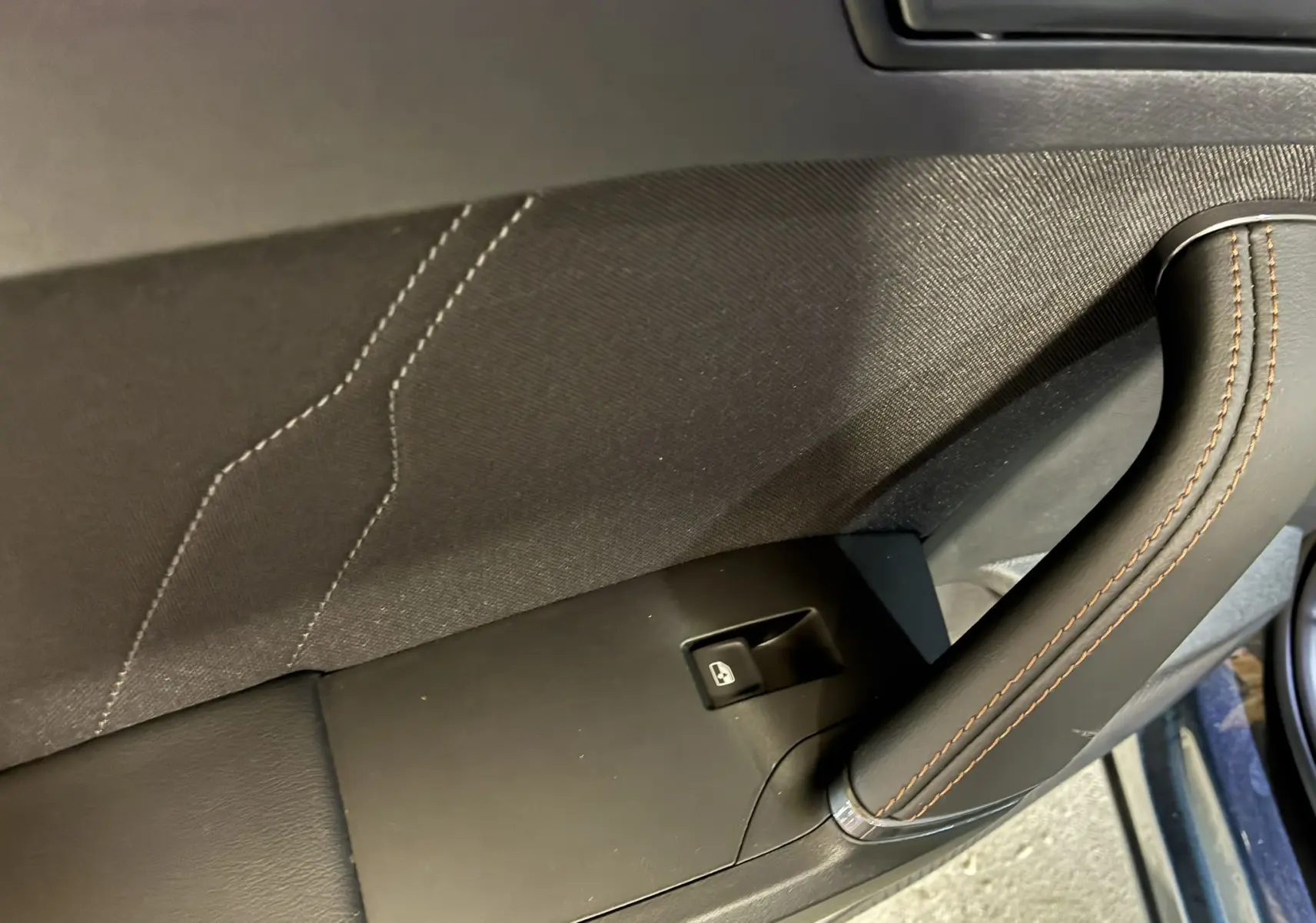 Gros plan sur la poignée intérieure en cuir noir avec surpiqûres marron et bouton de lève-vitre du côté gauche d'une CUPRA Formentor 2024.