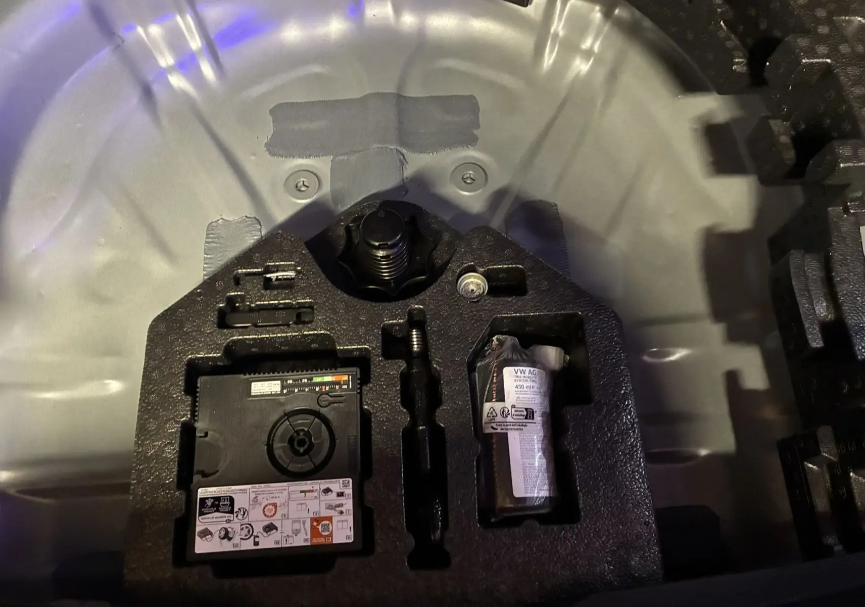 Gros plan sur le compartiment de rangement sous le coffre d’un CUPRA Formentor gris foncé 2024, montrant kit de réparation pneus.