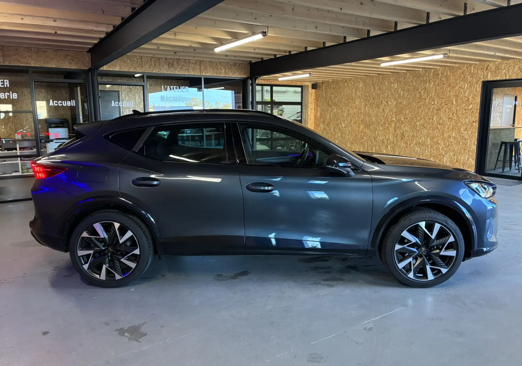 Vue latérale droite du CUPRA Formentor gris foncé 2024 en hybride essence, avec jantes bi-ton et feux arrière allumés.