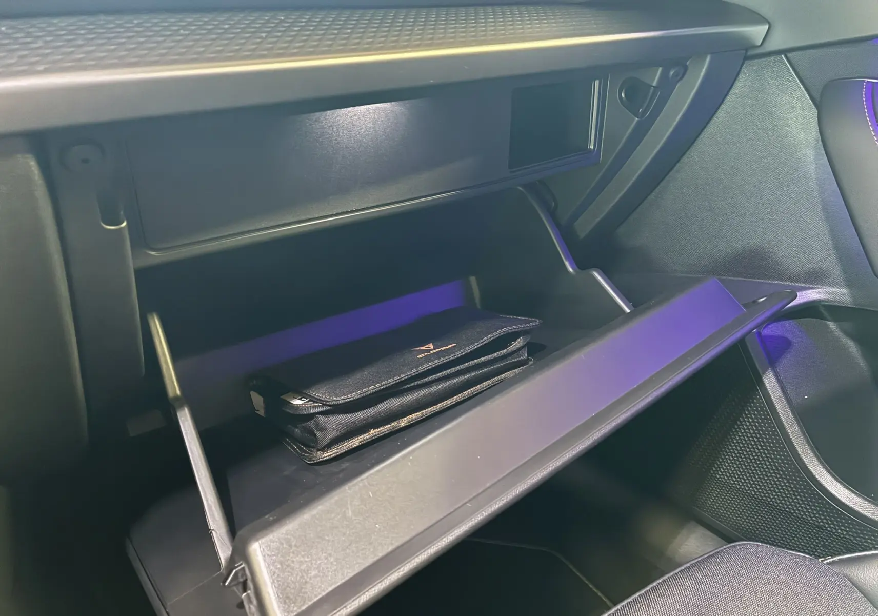 Gros plan sur la boîte à gants ouverte du CUPRA Formentor 2024, intérieur noir avec pochette siglée à l'intérieur.