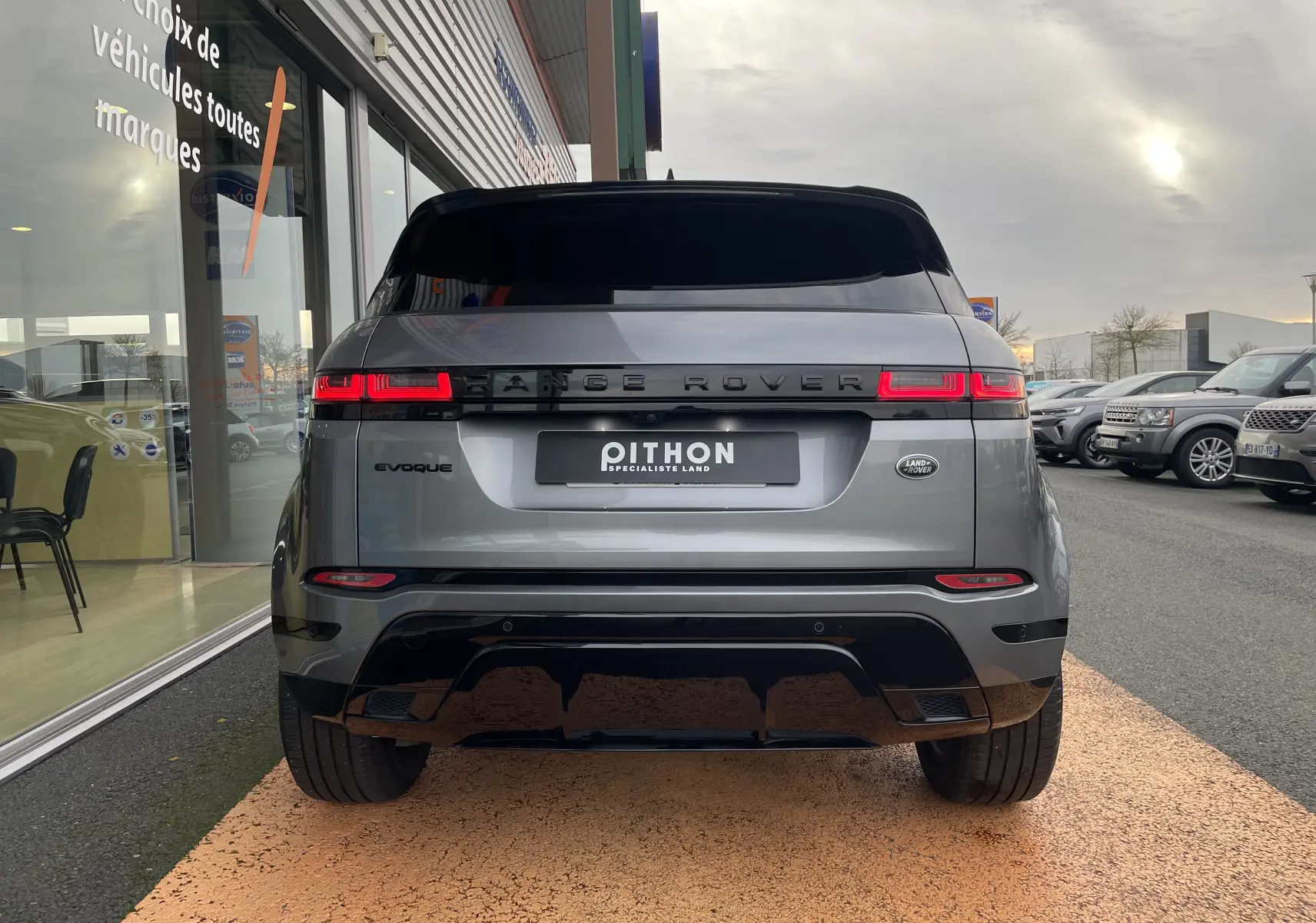Vue arrière d'un Range Rover Evoque 200D SE R-Dynamic gris Eiger avec feux LED allumés, stationné devant un showroom.
