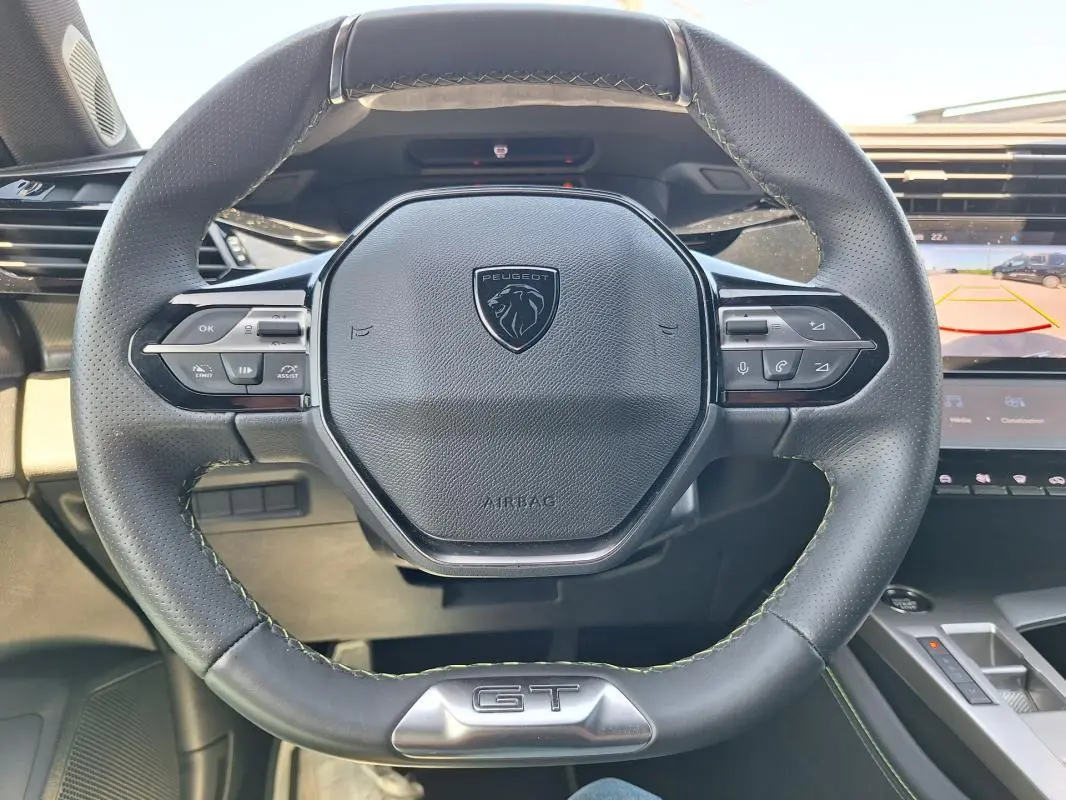 Vue rapprochée du volant cuir noir de la Peugeot 308 Hybrid 145 e-DCS6 GT avec logo et badge GT visible.