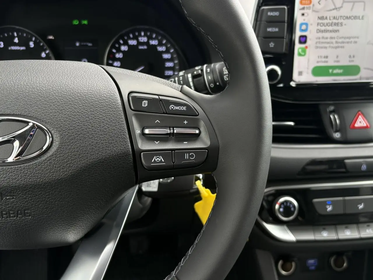 Gros plan sur le volant cuir côté gauche et tableau de bord avec écran tactile affichant Apple CarPlay dans une Hyundai i30 SW gris argent 2025.