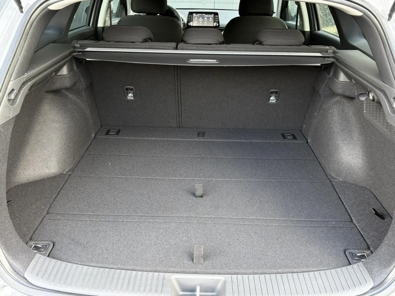 Vue intérieure du coffre spacieux d'une Hyundai i30 SW T-GDI 120 Modern gris argent avec cache-bagages déployé.