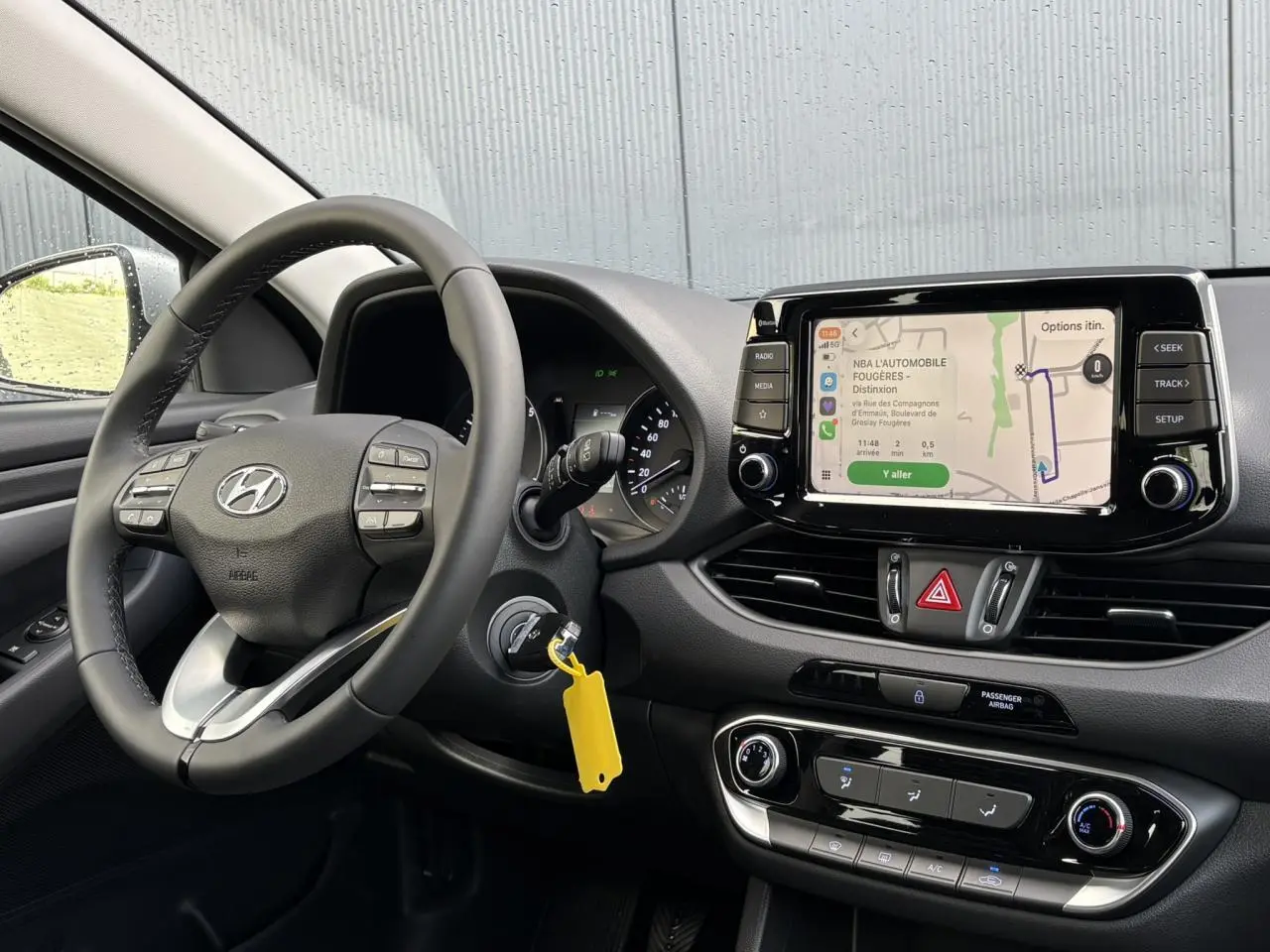 Vue intérieure côté conducteur du tableau de bord gris avec volant cuir et écran tactile affichant la navigation.