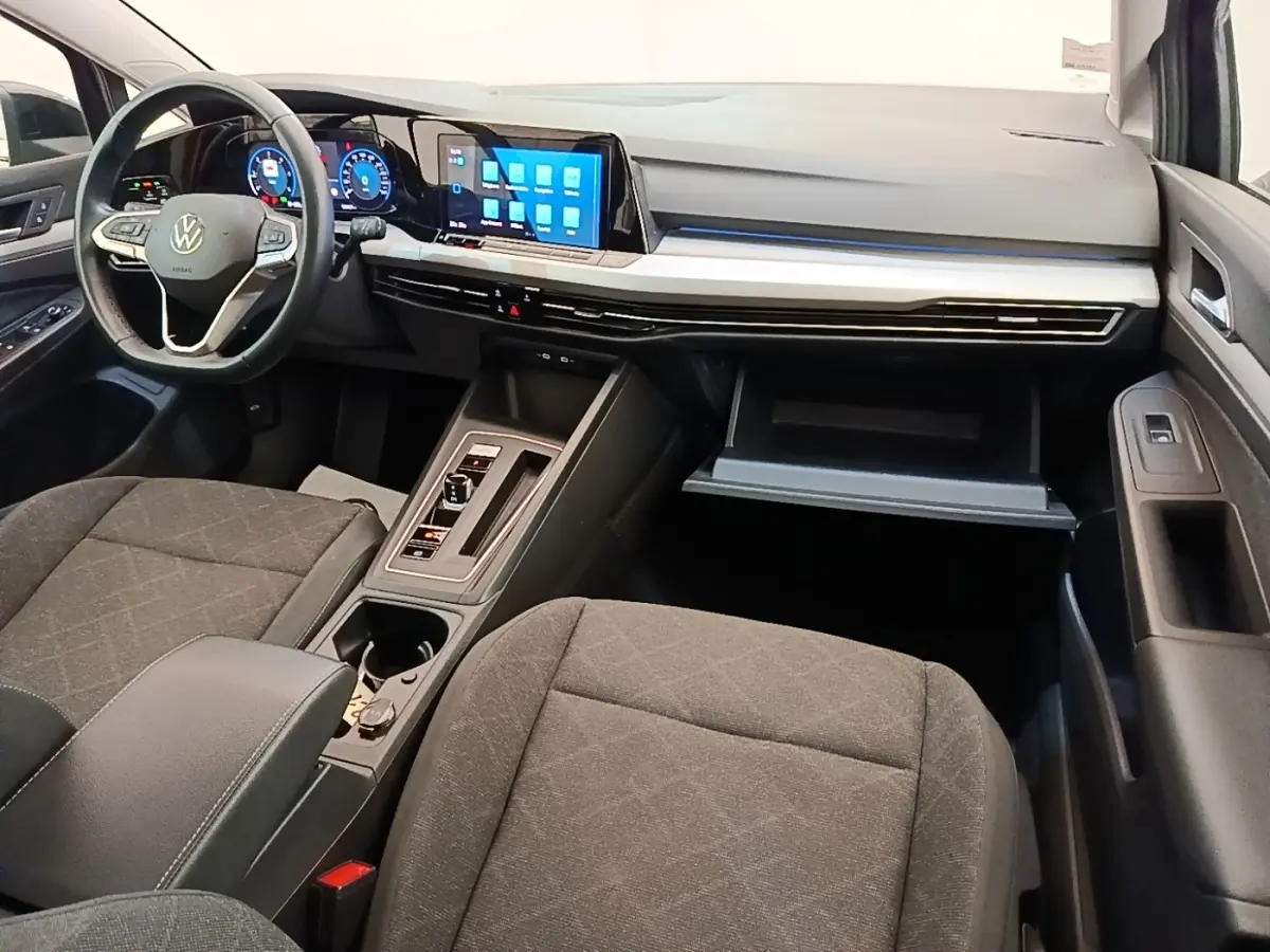 Intérieur avant de la Volkswagen Golf 2023, vue côté passager, tableau de bord noir avec écran tactile et volant cuir.