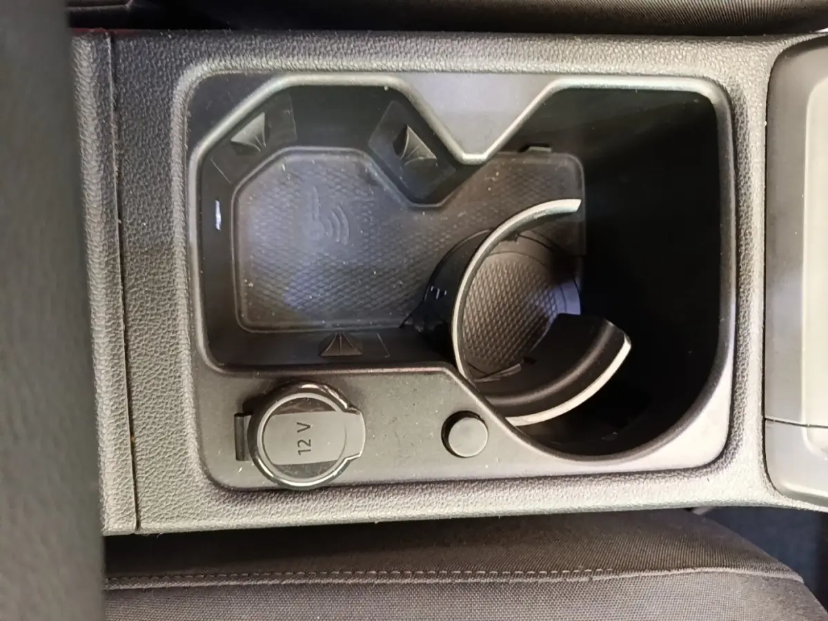Vue rapprochée de la console centrale noire d’une Volkswagen Golf 2023, avec prise 12V et zone de recharge sans fil.