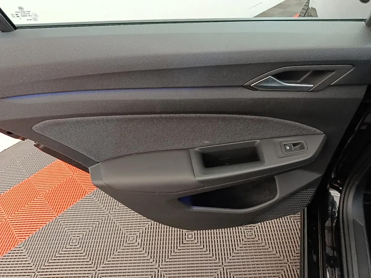 Vue intérieure de la porte côté conducteur d'une Volkswagen Golf noire 2023, avec habillage tissu et plastique noir.