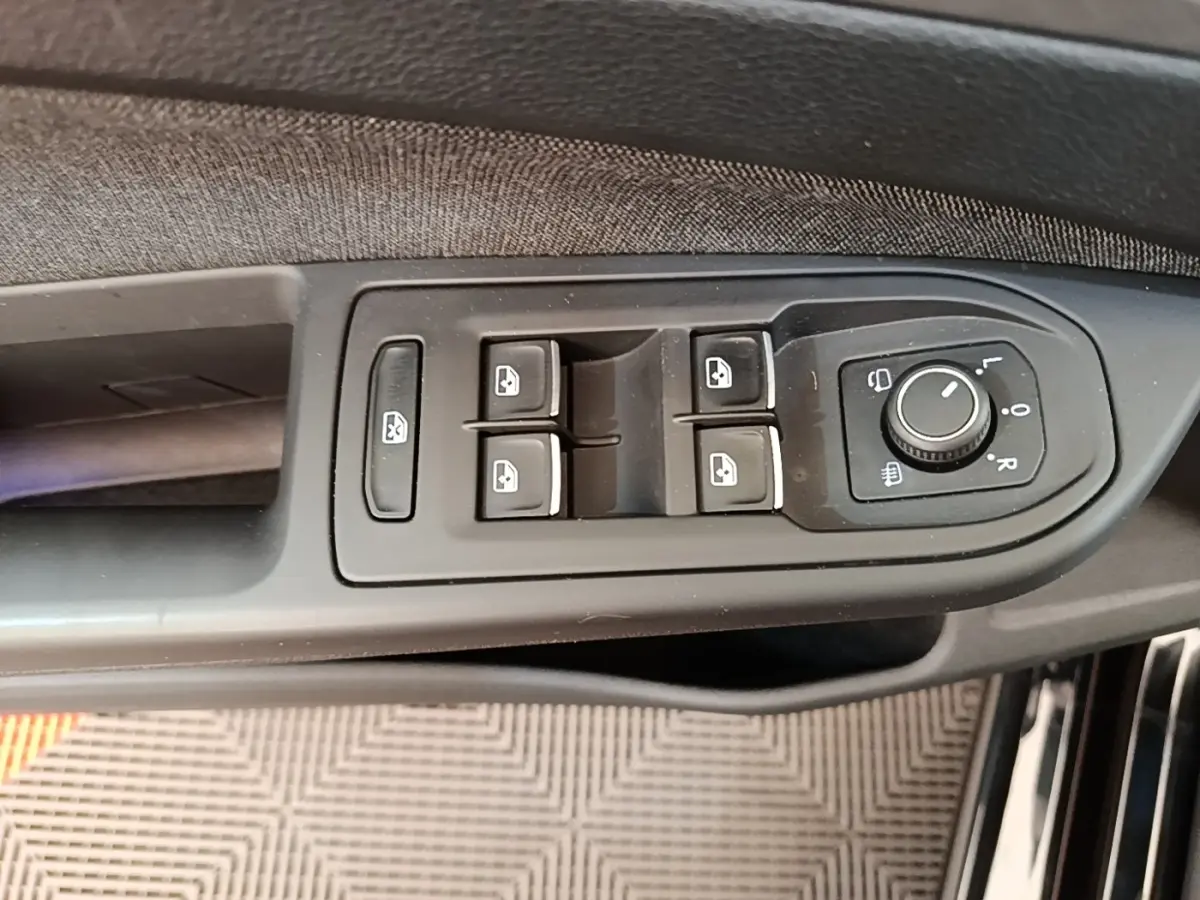 Gros plan sur les commandes de lève-vitres et rétroviseurs côté conducteur d'une Volkswagen Golf noire 2023.
