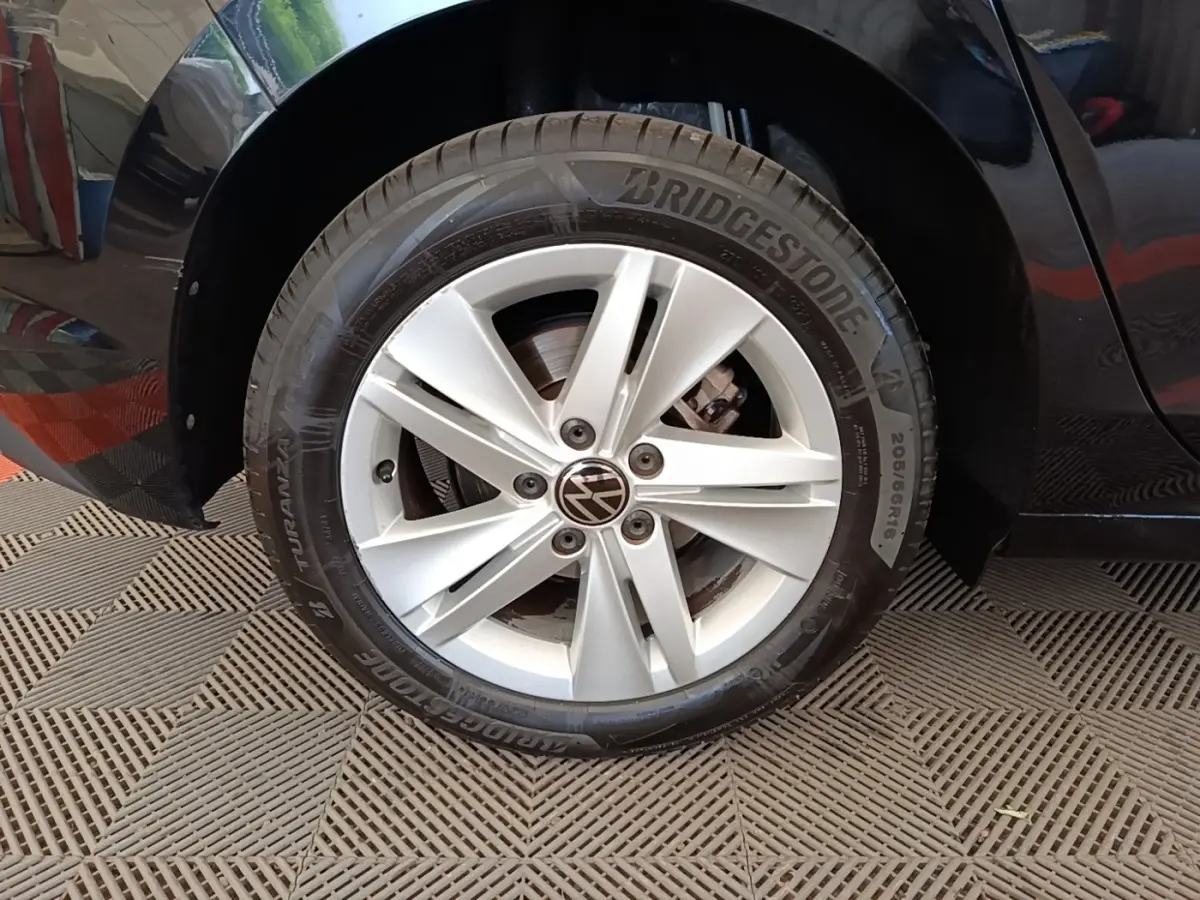 Gros plan sur la roue avant gauche d'une Volkswagen Golf noire, jante alliage argentée avec logo VW central.