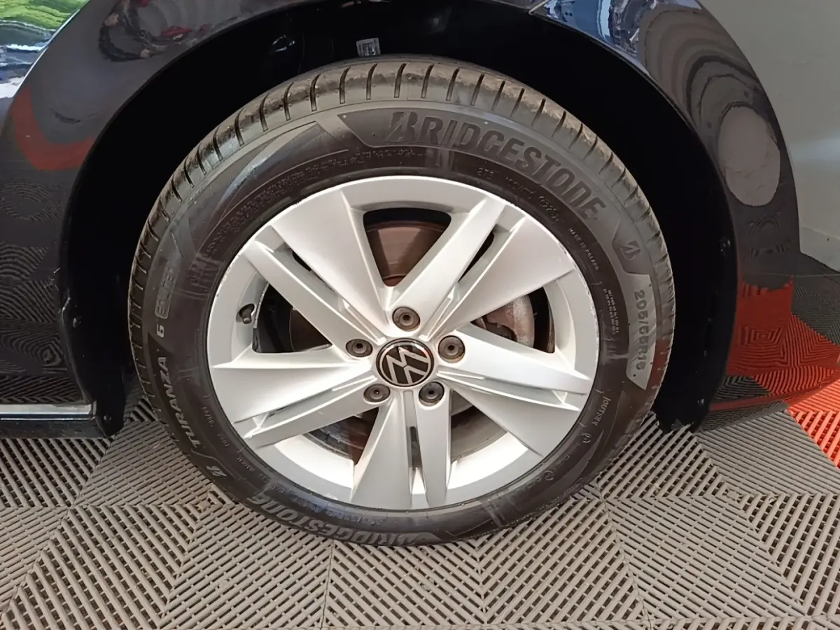 Gros plan sur la roue avant droite d'une Volkswagen Golf noire, jante alliage argentée avec logo VW central.