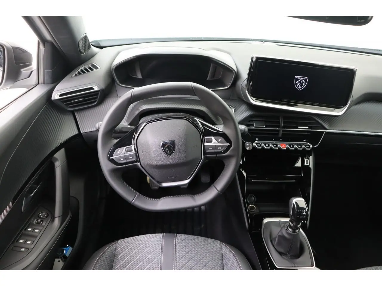 Vue intérieure centrée sur le volant et la console centrale du Peugeot 2008 blanc Okenite avec boîte manuelle.