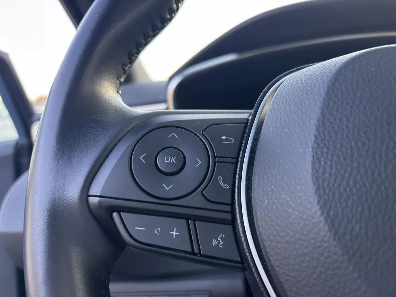 Gros plan sur les commandes multifonctions à gauche du volant en cuir noir de la Toyota Corolla hybride bleu clair 2020.