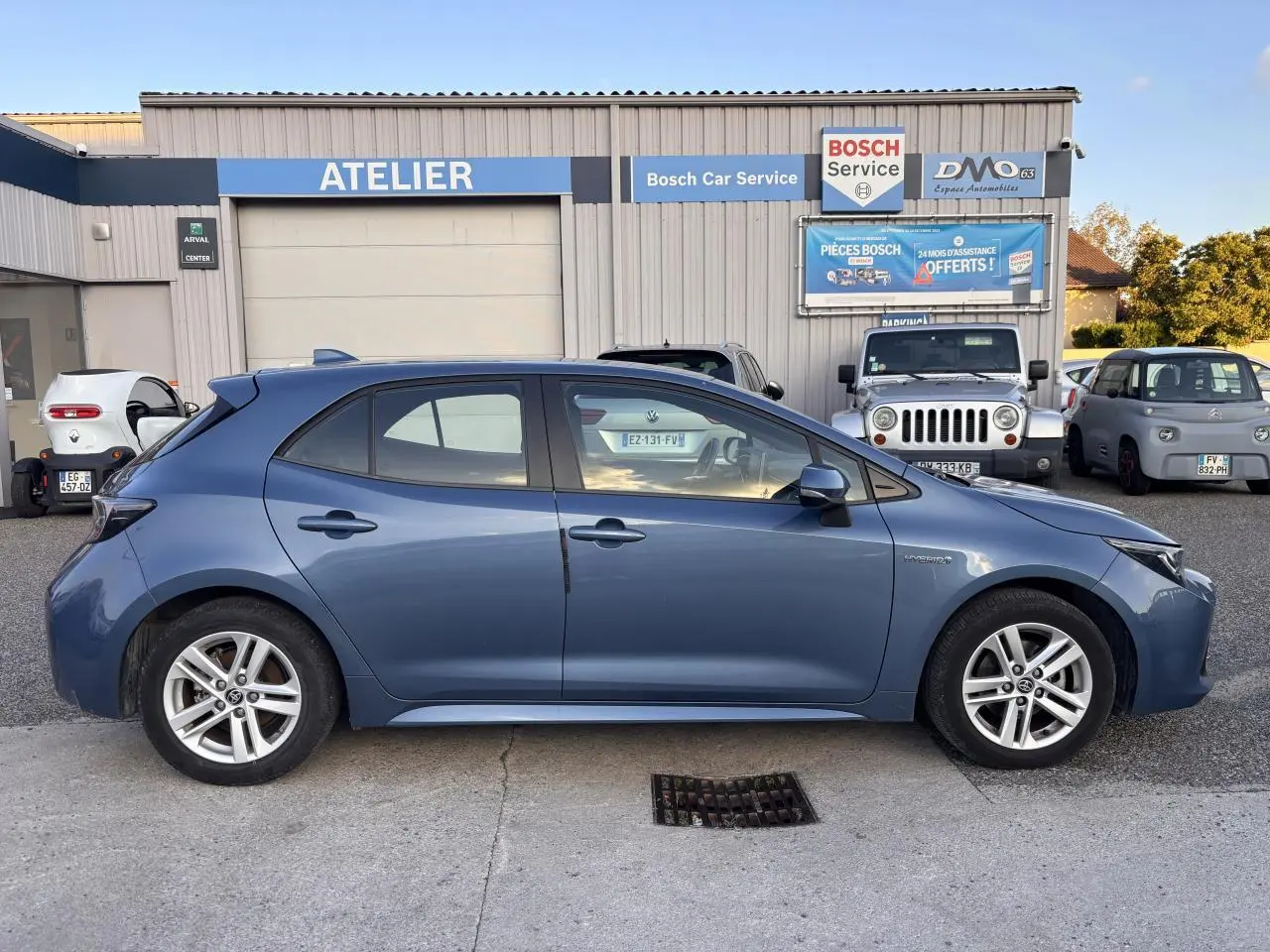 Profil côté gauche de la Toyota Corolla hybride 2020 bleu clair garée devant un atelier Bosch Car Service.