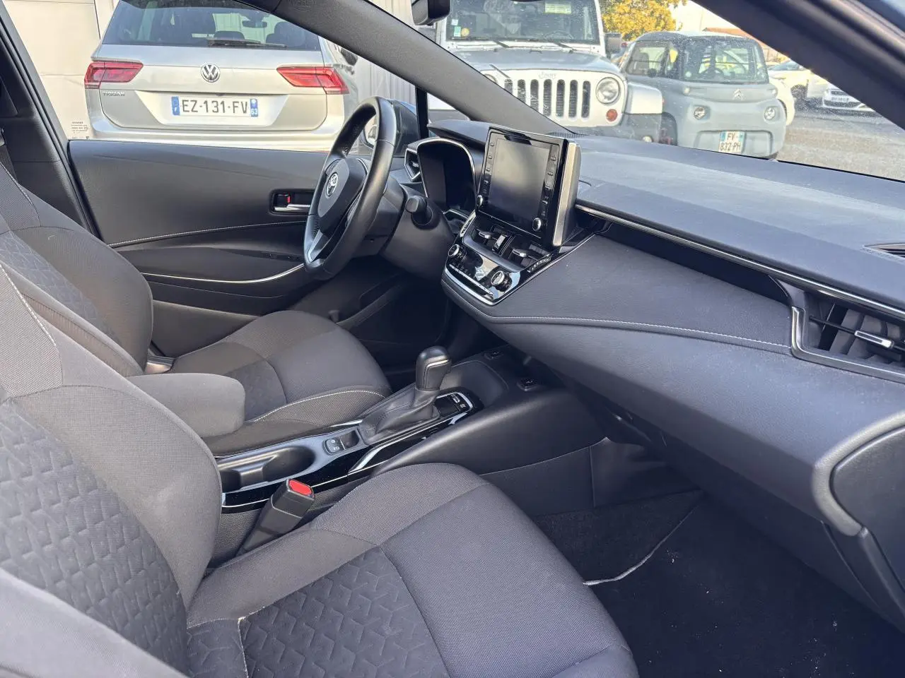Intérieur avant droit de la Toyota Corolla hybride 2020, montrant sièges noirs, volant, console centrale et écran tactile.