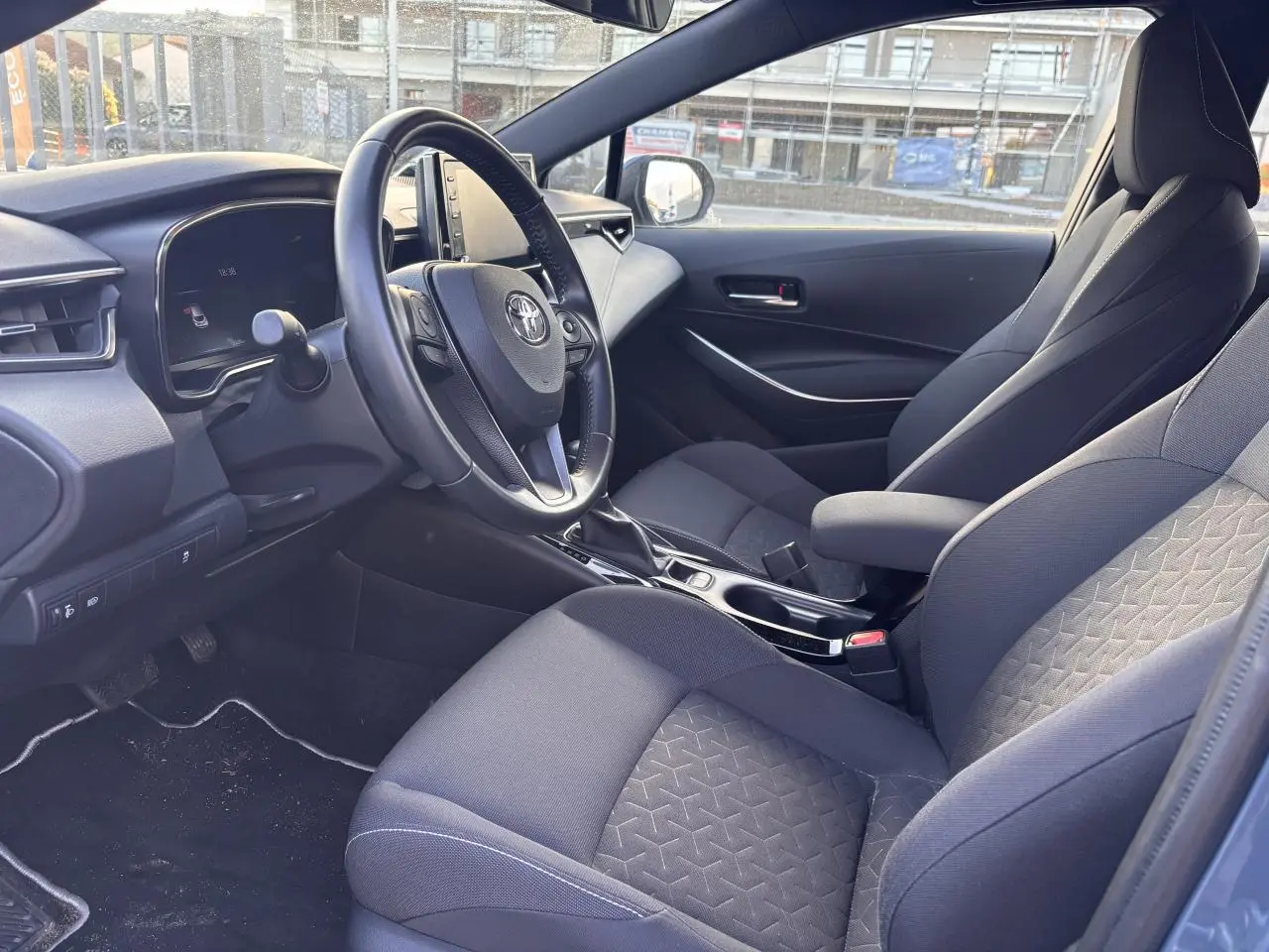 Intérieur de la Toyota Corolla hybride 2020 vu côté conducteur, sièges tissu gris et tableau de bord moderne.