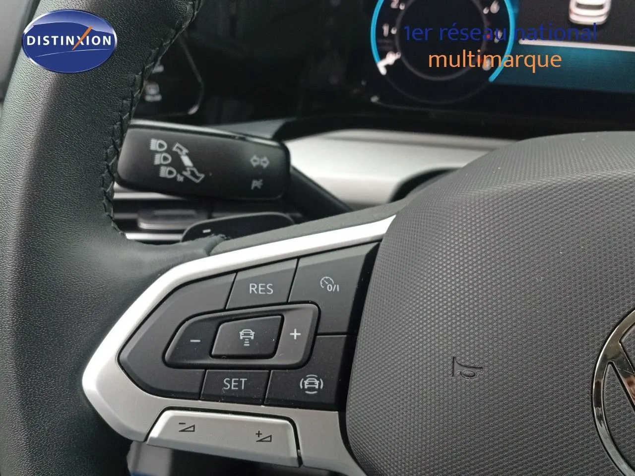 Gros plan sur le volant noir de la Volkswagen Golf VIII avec commandes intégrées et tableau de bord numérique en arrière-plan.