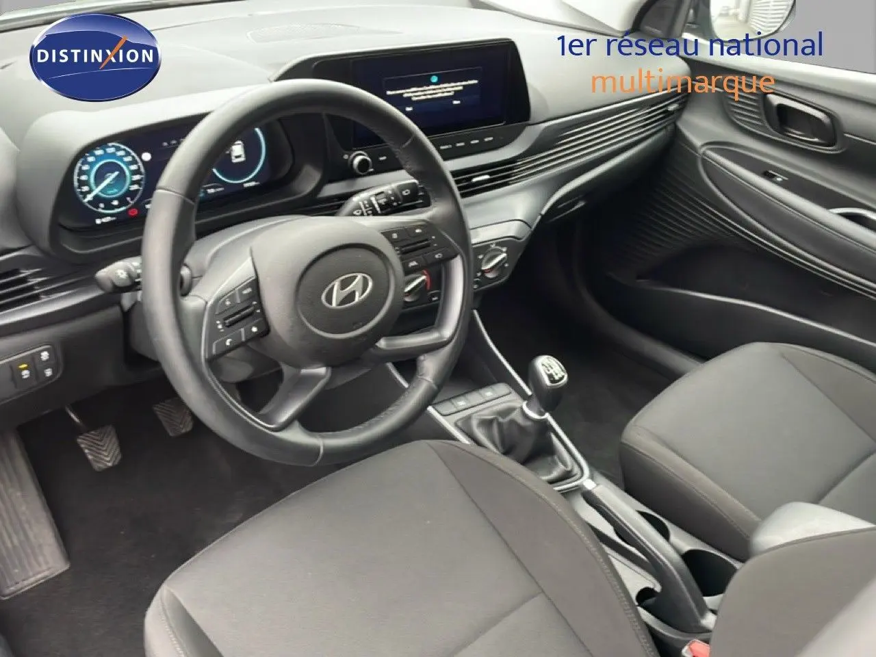 Vue intérieure de face côté conducteur de la Hyundai i20 2025 avec volant cuir noir et tableau de bord digital.