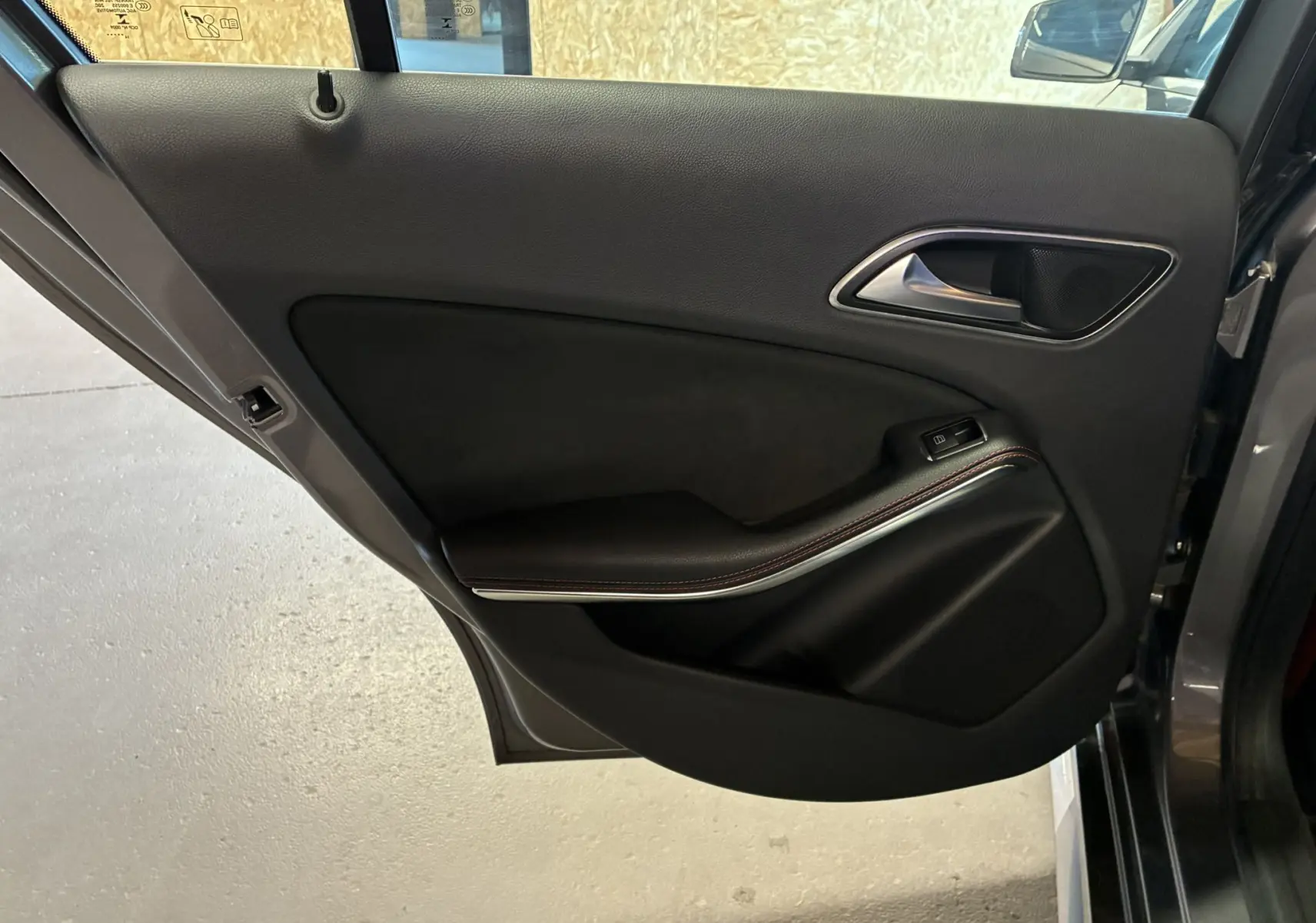 Vue intérieure de la porte arrière droite d'une Mercedes Classe A 250 AMG Sport gris avec garniture noire et poignée métal.