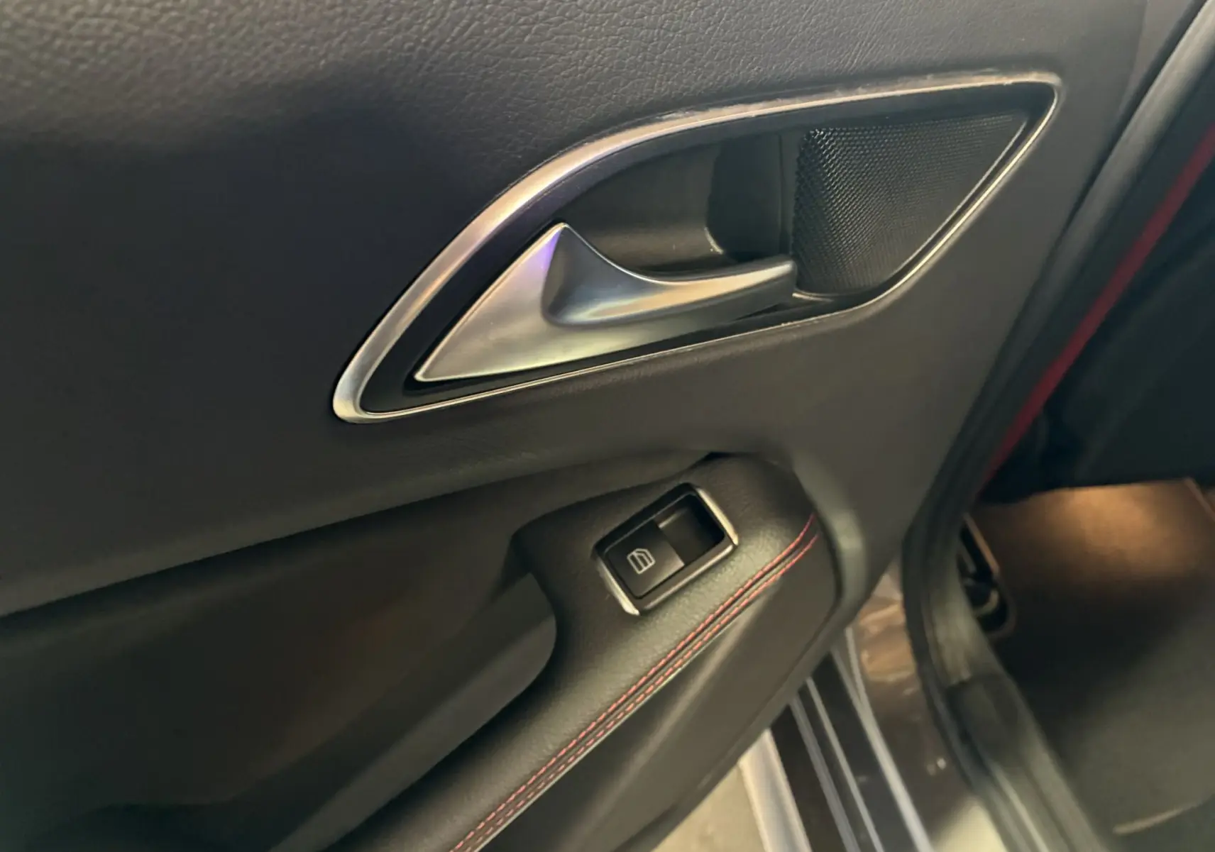Gros plan sur la poignée intérieure côté gauche en cuir noir avec surpiqûres rouges d'une Mercedes Classe A 250 AMG Sport gris.