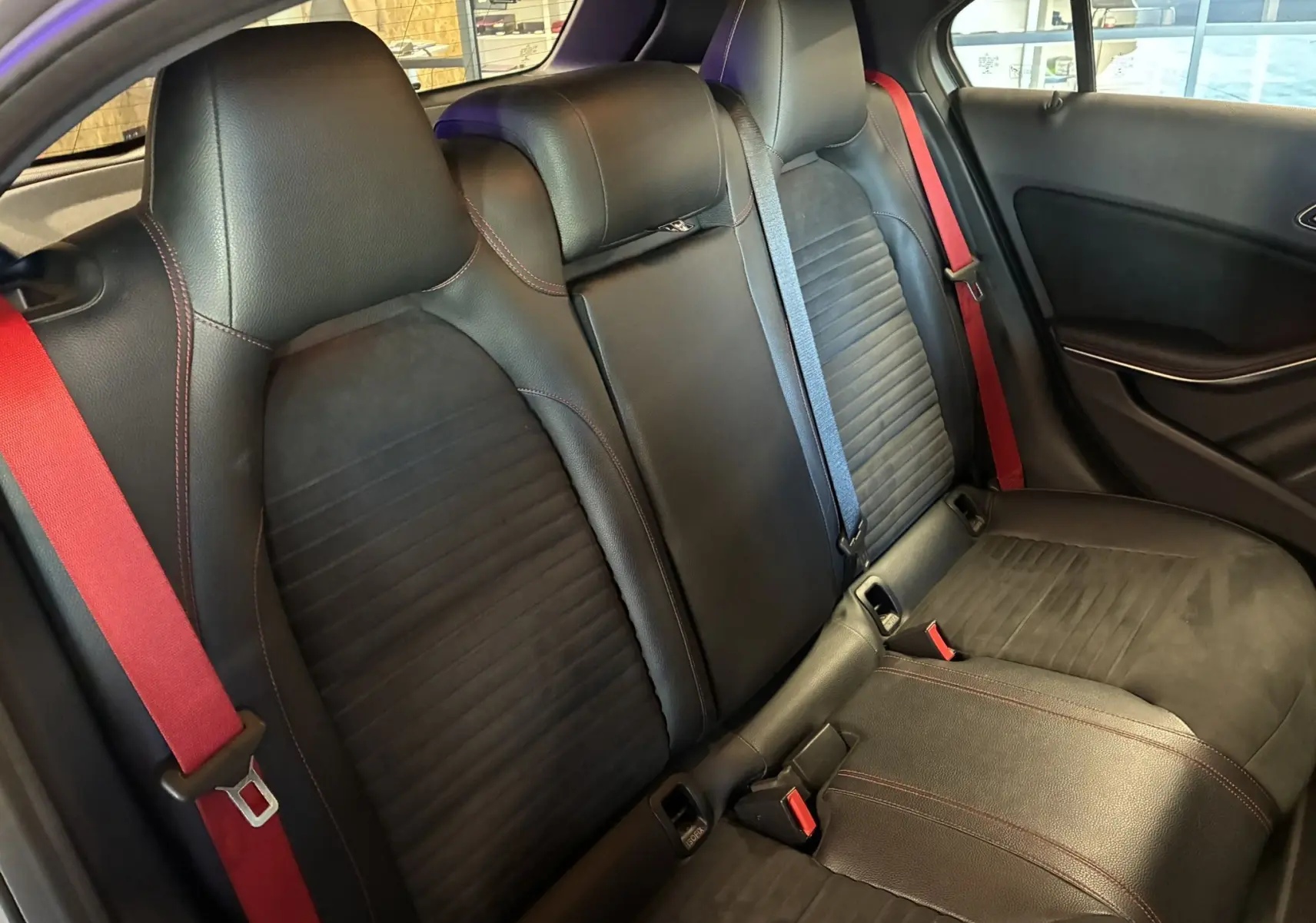 Vue intérieure arrière des sièges noirs en cuir et alcantara d'une Mercedes Classe A 250 AMG Sport avec ceintures rouges.