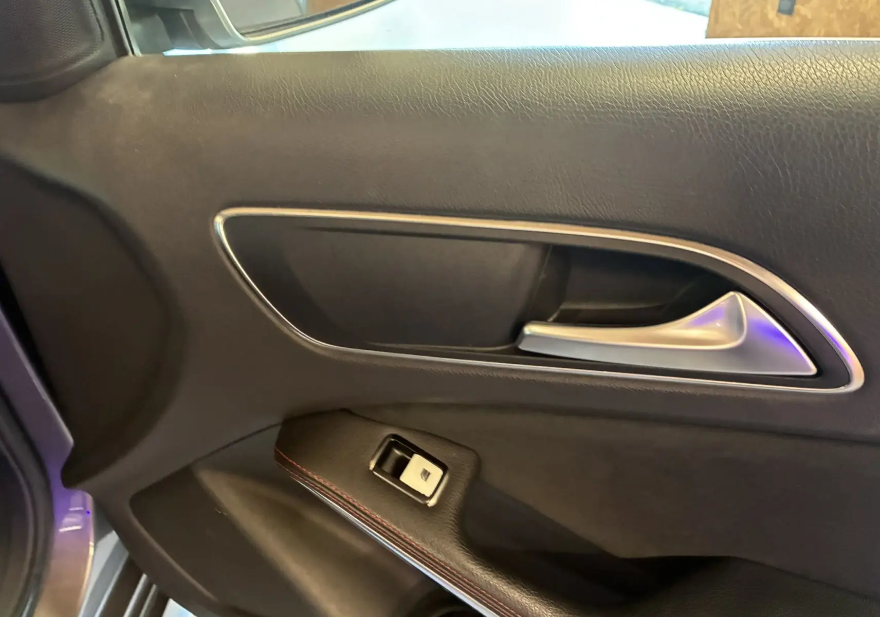 Poignée de porte intérieure côté gauche en cuir noir avec surpiqûres rouges dans une Mercedes Classe A 250 AMG Sport gris 2014.