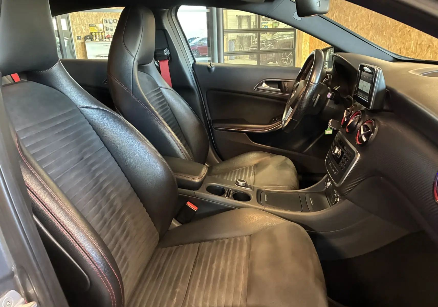 Vue intérieure côté conducteur de la Mercedes Classe A 250 AMG Sport 2014 avec sièges cuir noir et détails rouges.