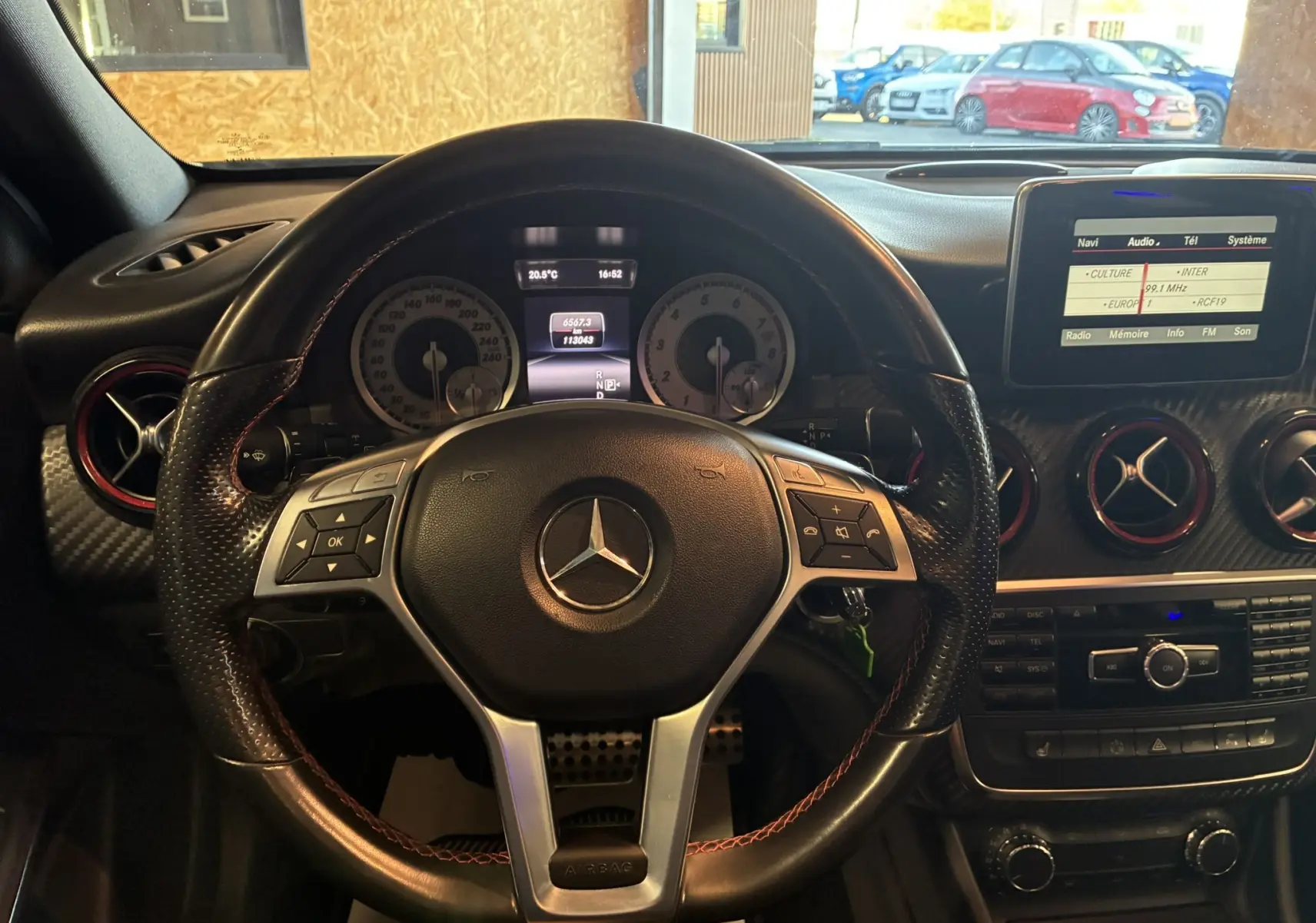 Vue intérieure centrée sur le volant cuir noir de la Mercedes Classe A 250 AMG Sport, avec tableau de bord et écran multimédia allumé.