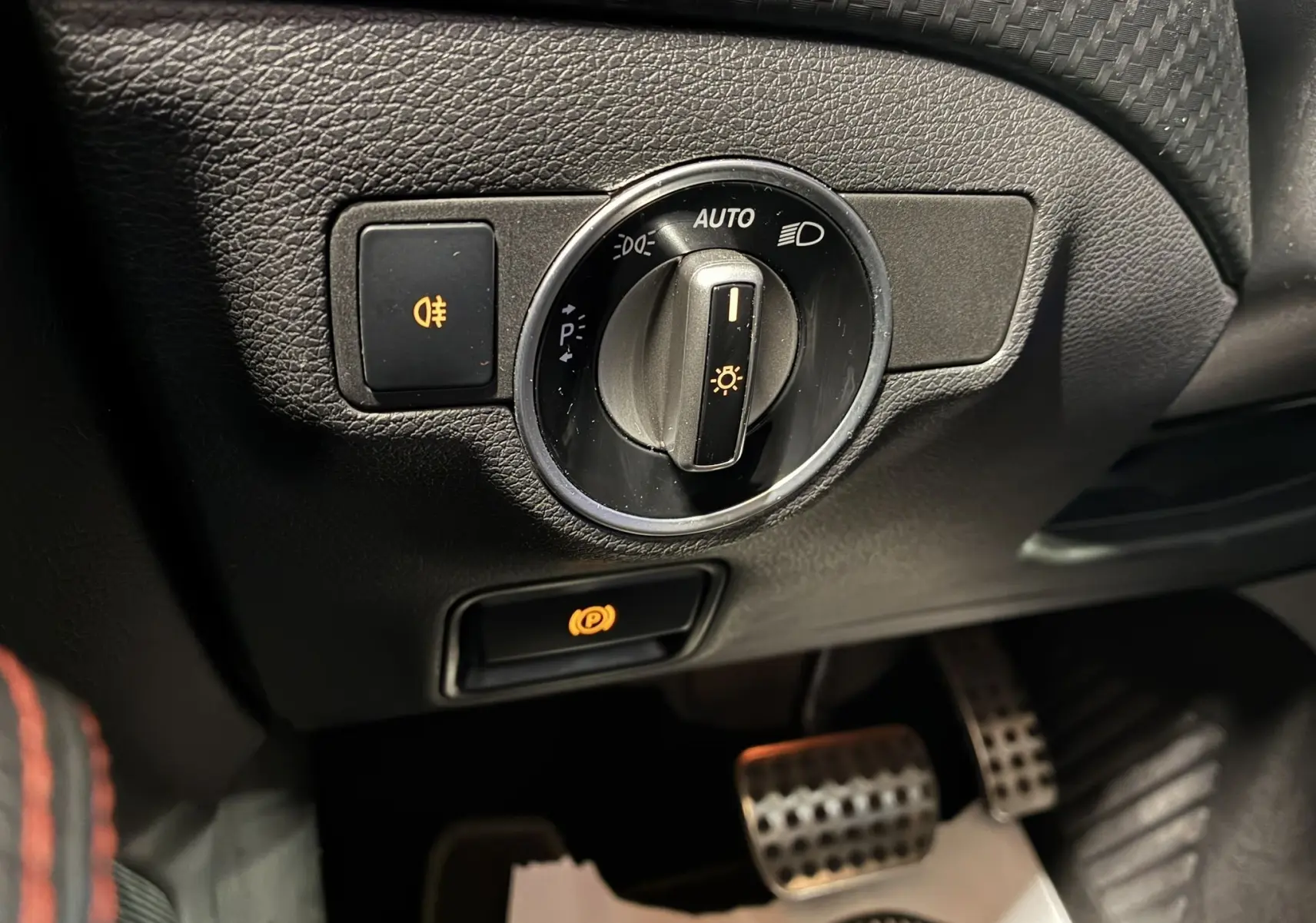 Gros plan sur le bouton de commande des phares et frein à main électrique dans l'habitacle noir de la Mercedes Classe A 250 AMG Sport 2014.